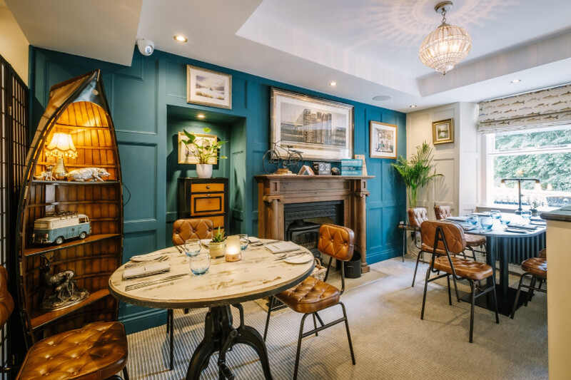 Dining room with teal panelled walls, a fireplace and round tables at 1863, Ullswater