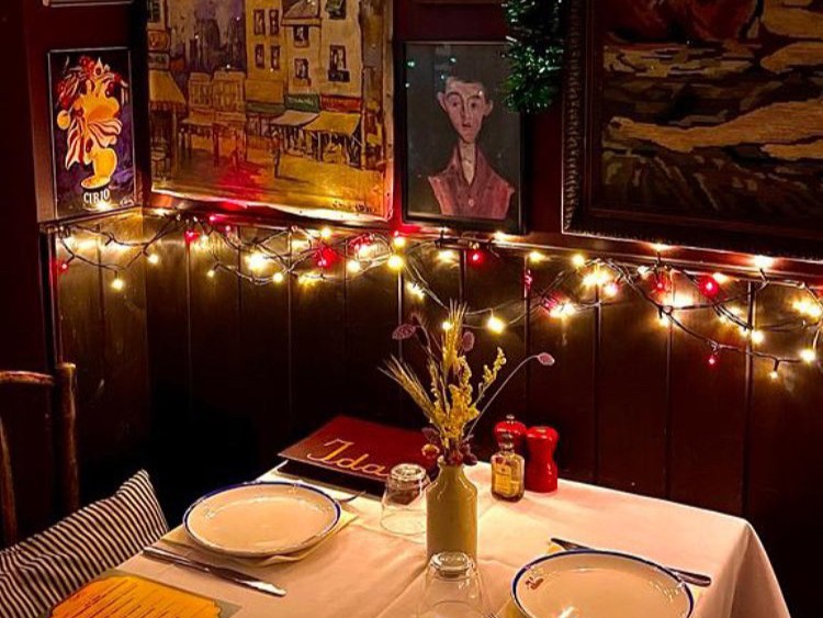 Ida, Kilburn, London — cosy candlelit corner table with fairy lights, eclectic vintage artwork and rustic charm — London regional winner, Best Local Restaurant 2025 in The Good Food Guide.