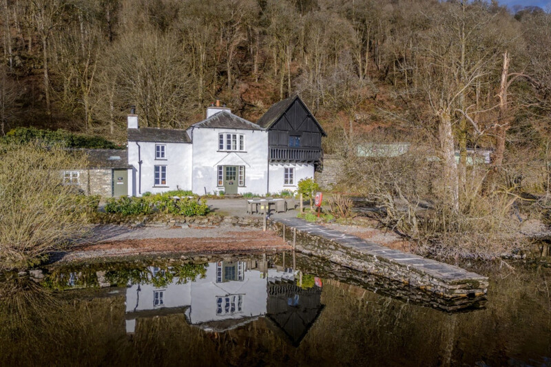 White lakeside cottage and jetty reflected in Windermere at Low Strawberry Gardens, Hawkshead