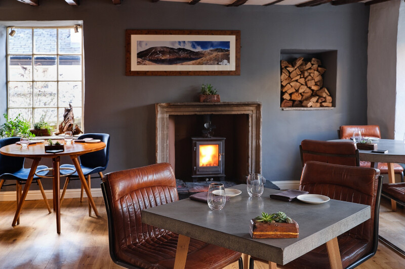 Dining room with a stone fireplace, log store and mountain painting at Rogan & Co, Cartmel